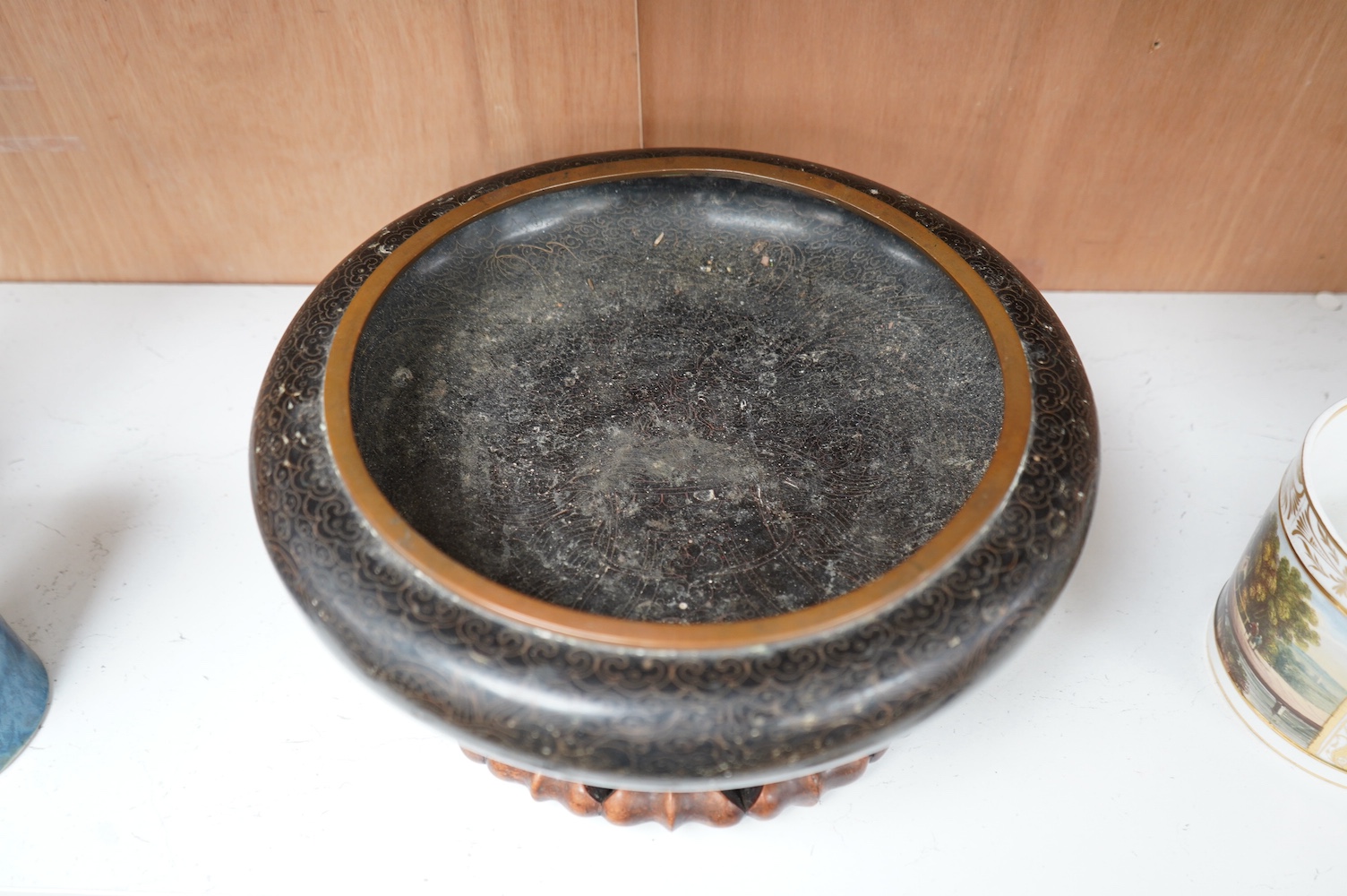 A Chinese black ground cloisonné enamel ‘dragon’ bowl on a carved hardwood stand, 14.5cm high. Condition - fair